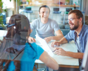 Three people sitting by a table smiling together with a bunch of papers on the table.