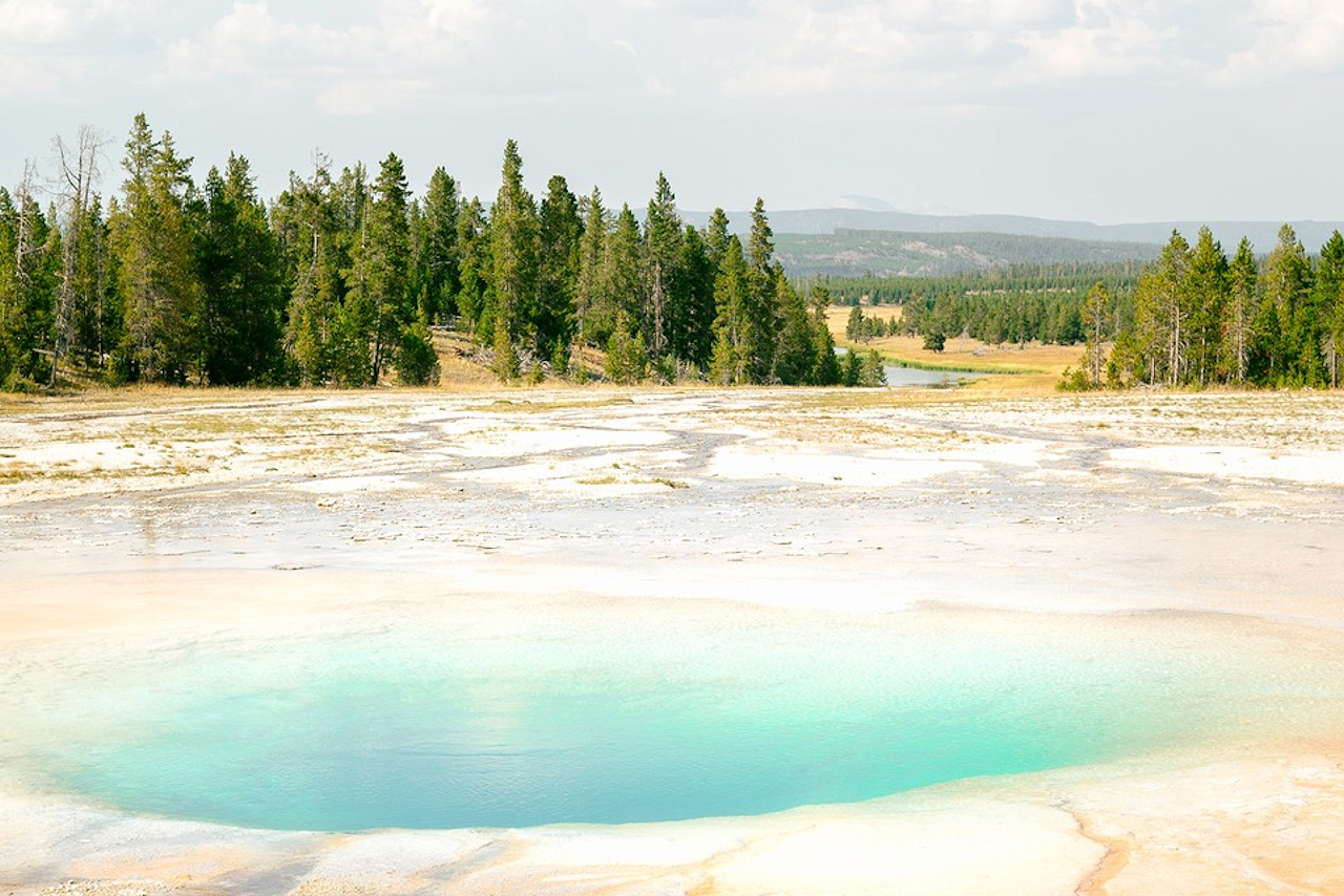 A beautiful image of Yellowstone, with clear blue water and trees all around.