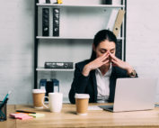 A woman wearing corporate attire sitting by an office desk looking stressed out.