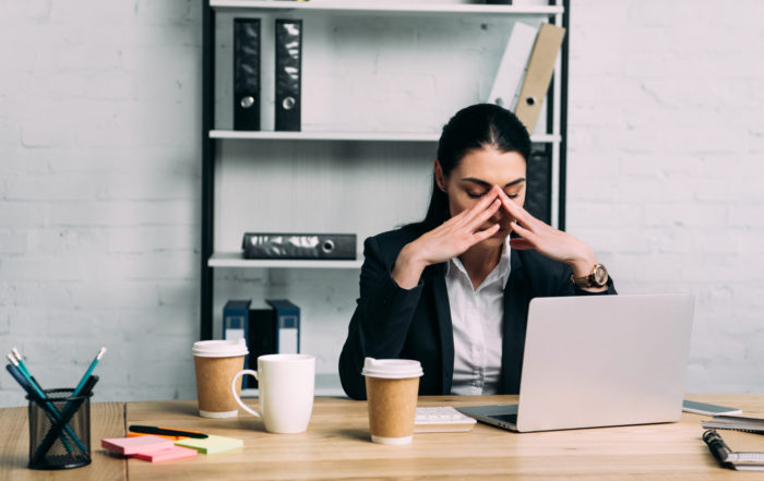 A woman wearing corporate attire sitting by an office desk looking stressed out.