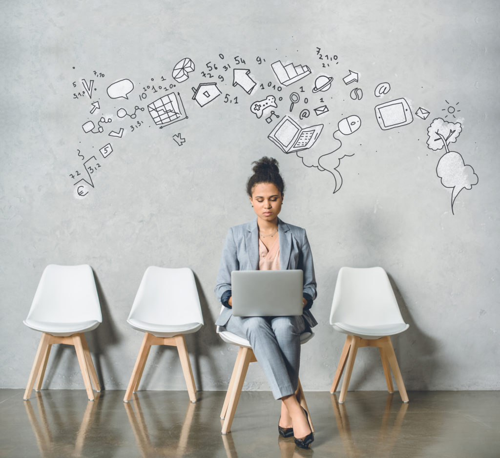 A woman wearing corporate attire sitting on a white chair with her laptop on her lap.