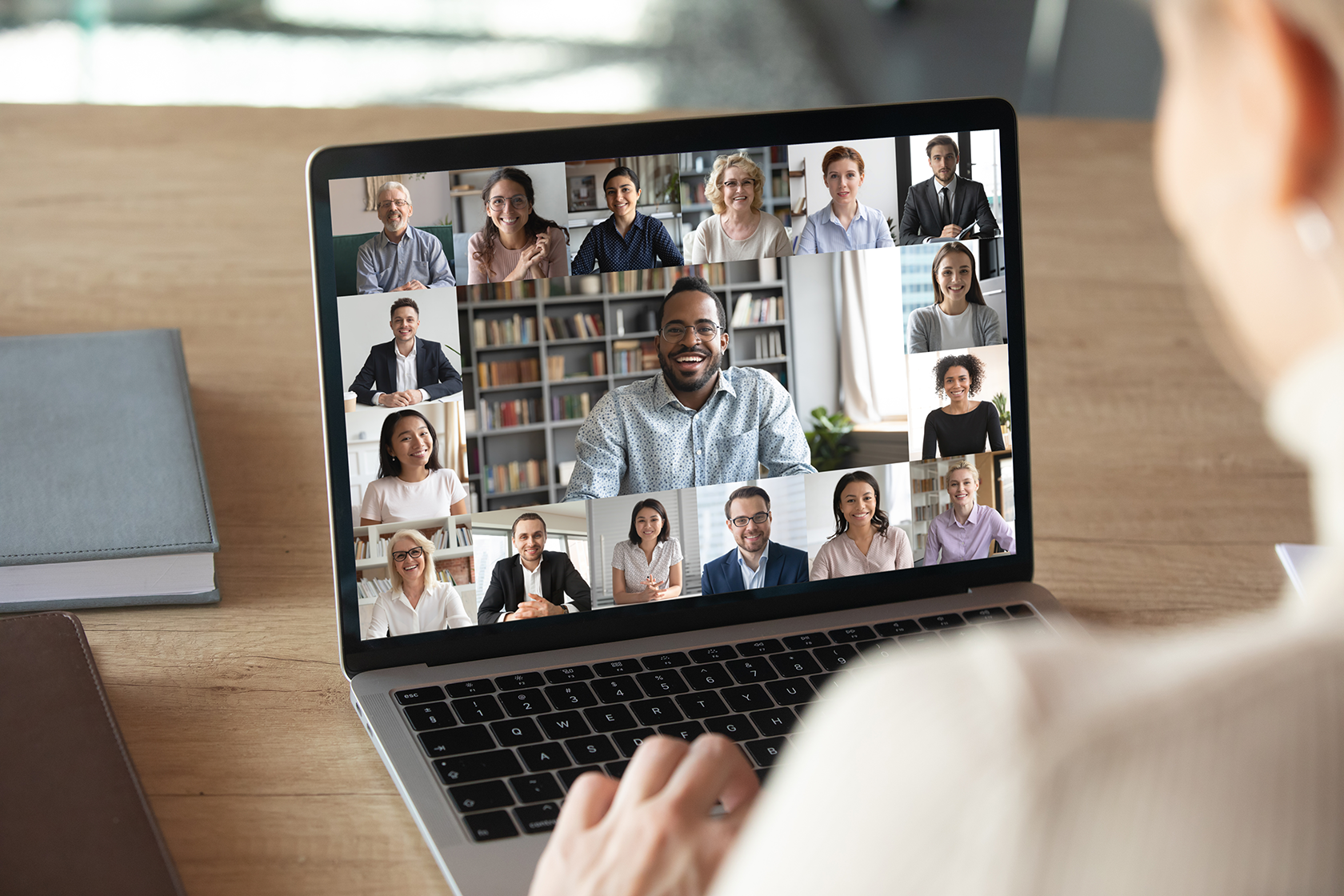 Someone looking at a laptop screen with multiple people on a virtual meeting.