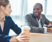 A man and a woman sitting together by a conference table talking and smiling.